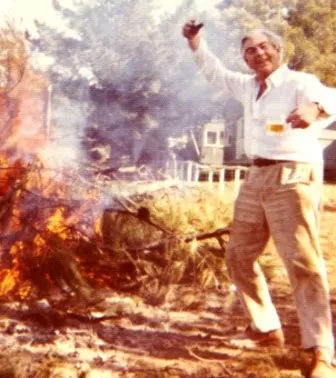 A man standing next to fire with a bottle of wine.