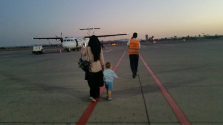 A woman and child walking across the tarmac of an airport.