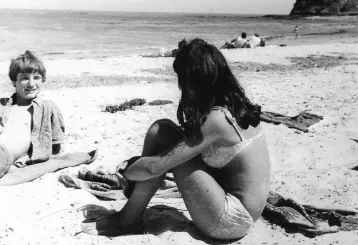 A woman sitting on the beach in her underwear.