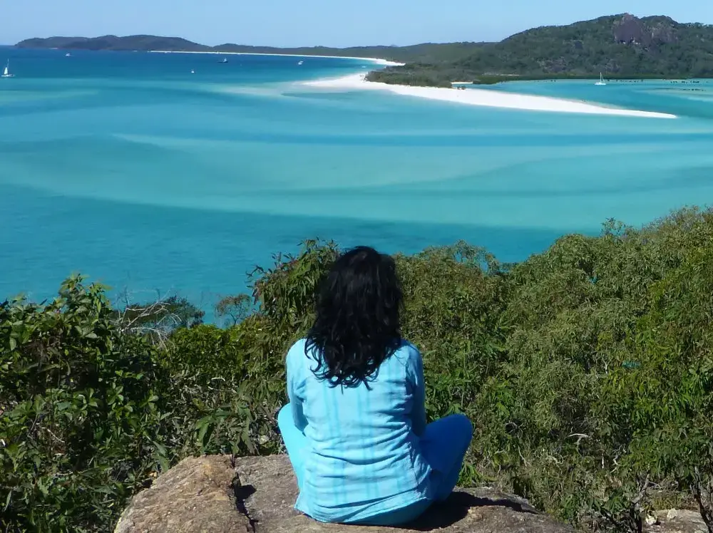 A woman sitting on top of a hill looking at the ocean.