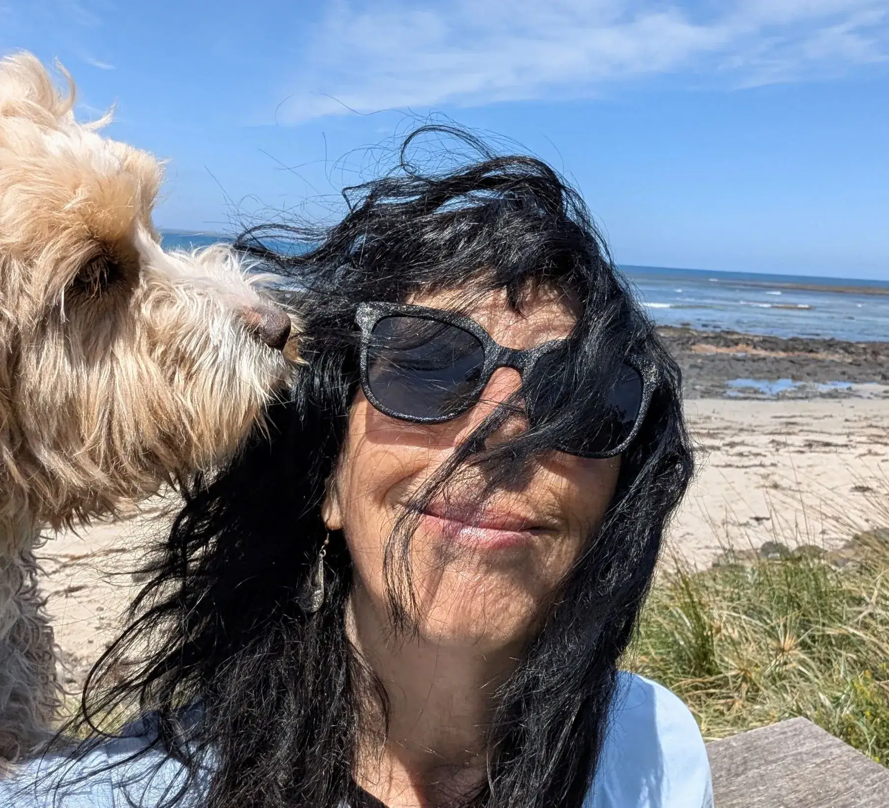 Woman with sunglasses nuzzled by dog at beach