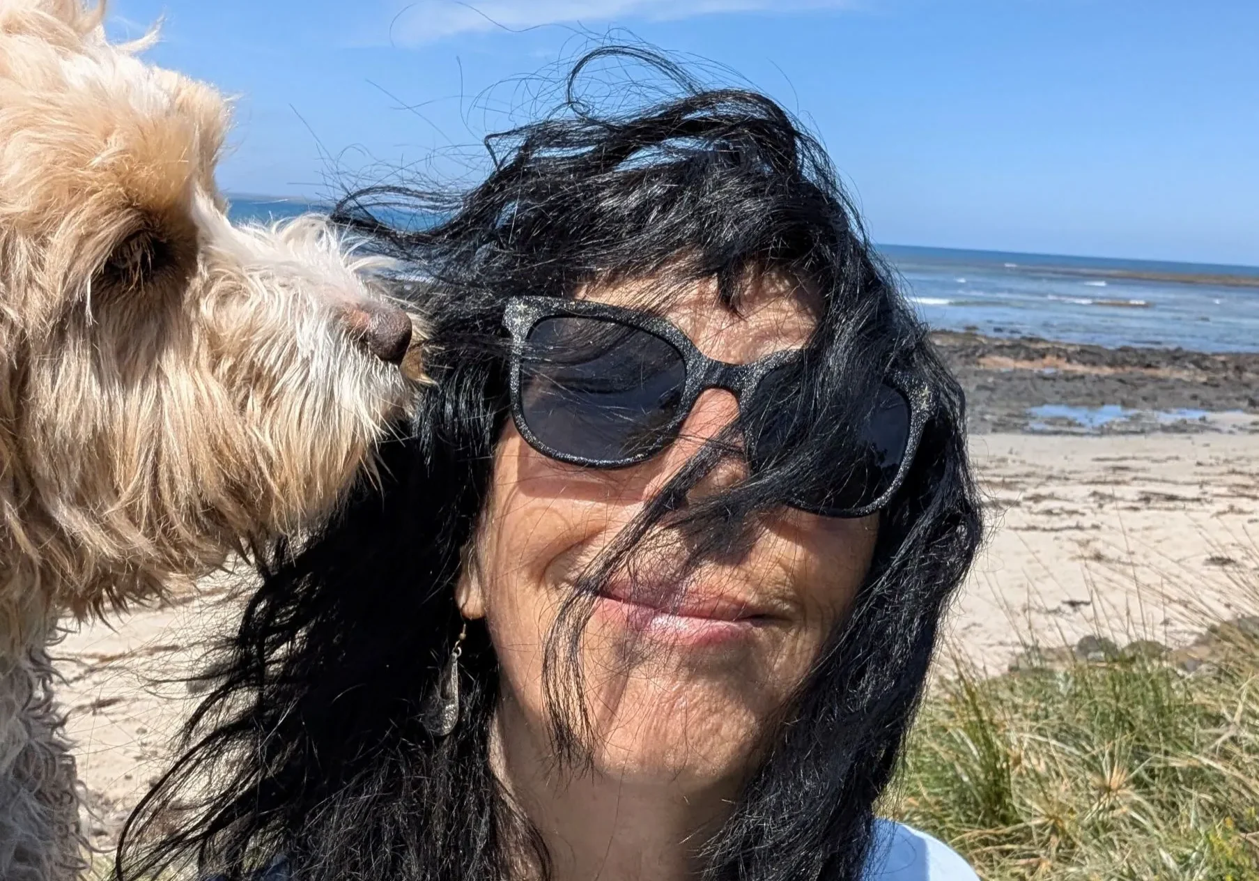 Woman with sunglasses nuzzled by dog at beach
