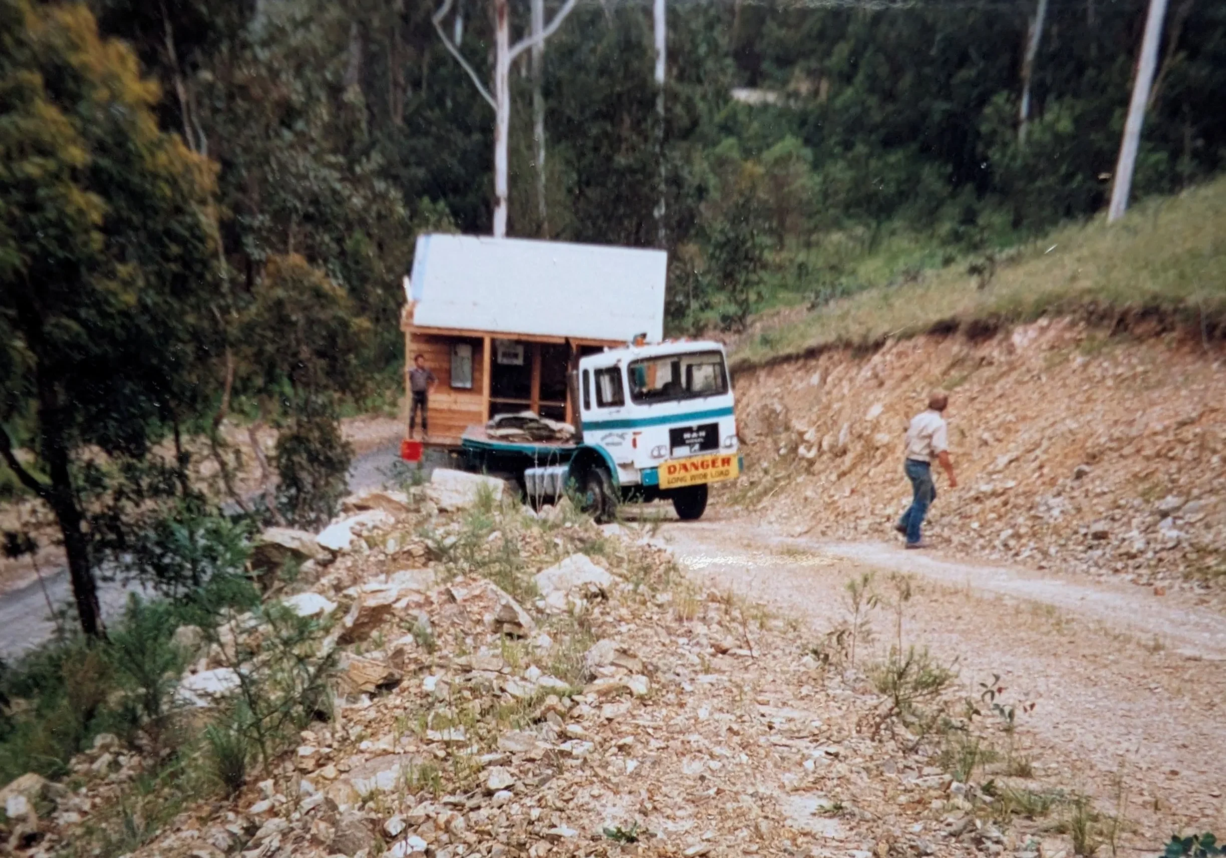 Truck carrying tiny cabin along rocky forest road