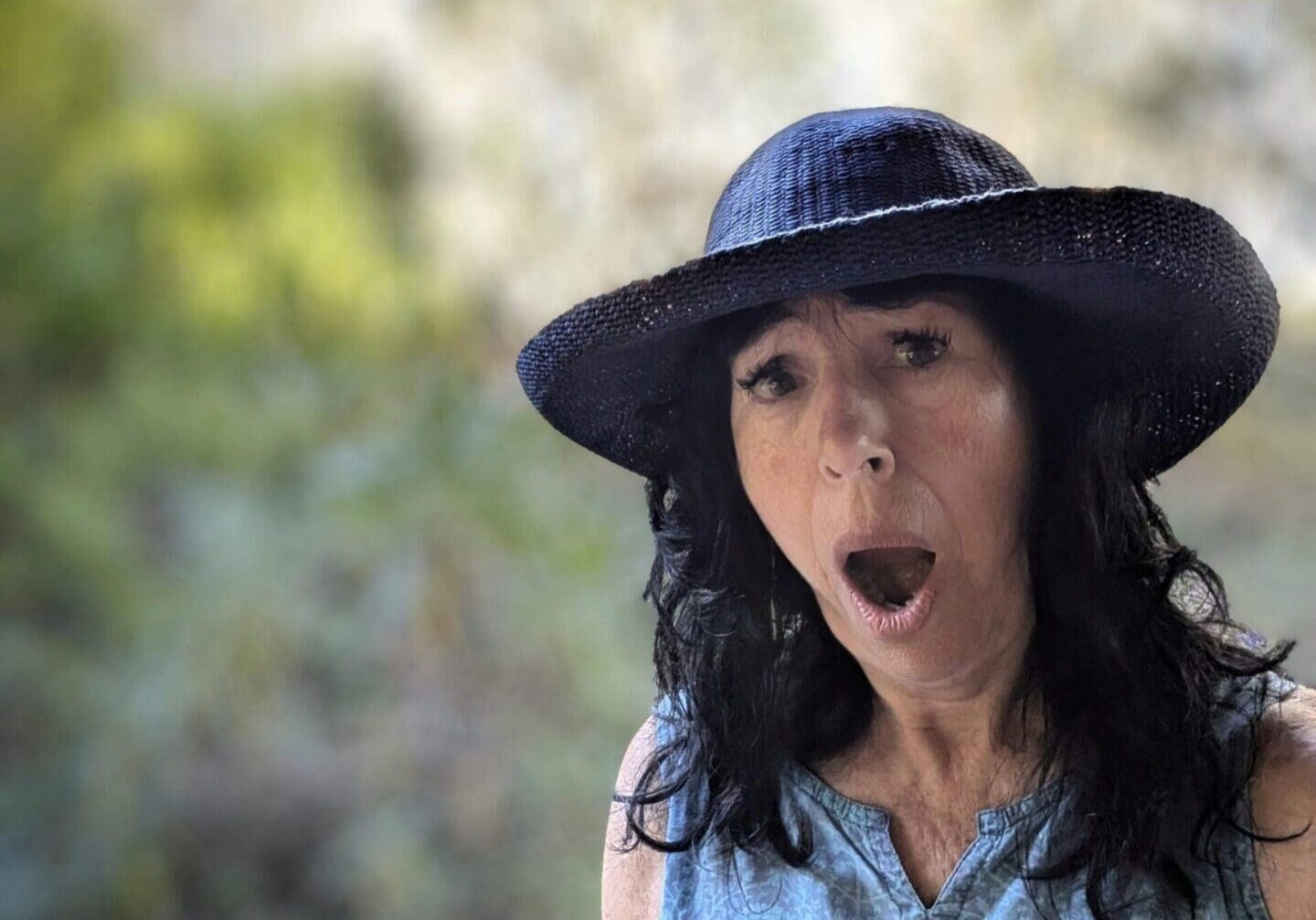 Woman wearing hat, surprised expression outdoors.