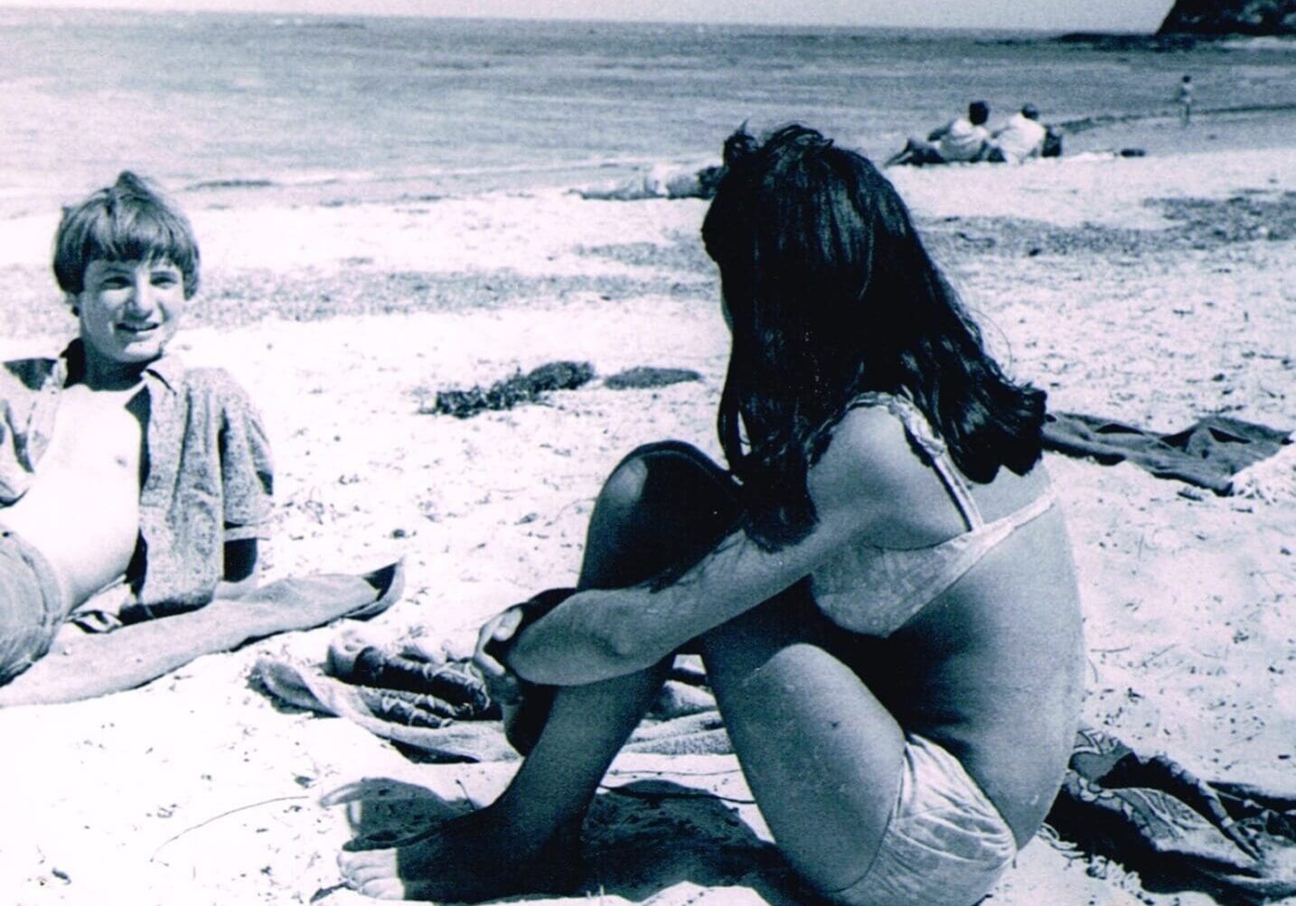 A woman sitting on the beach with a child.