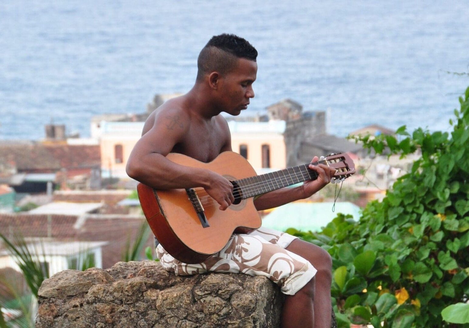 Man playing guitar on a rock outdoors.
